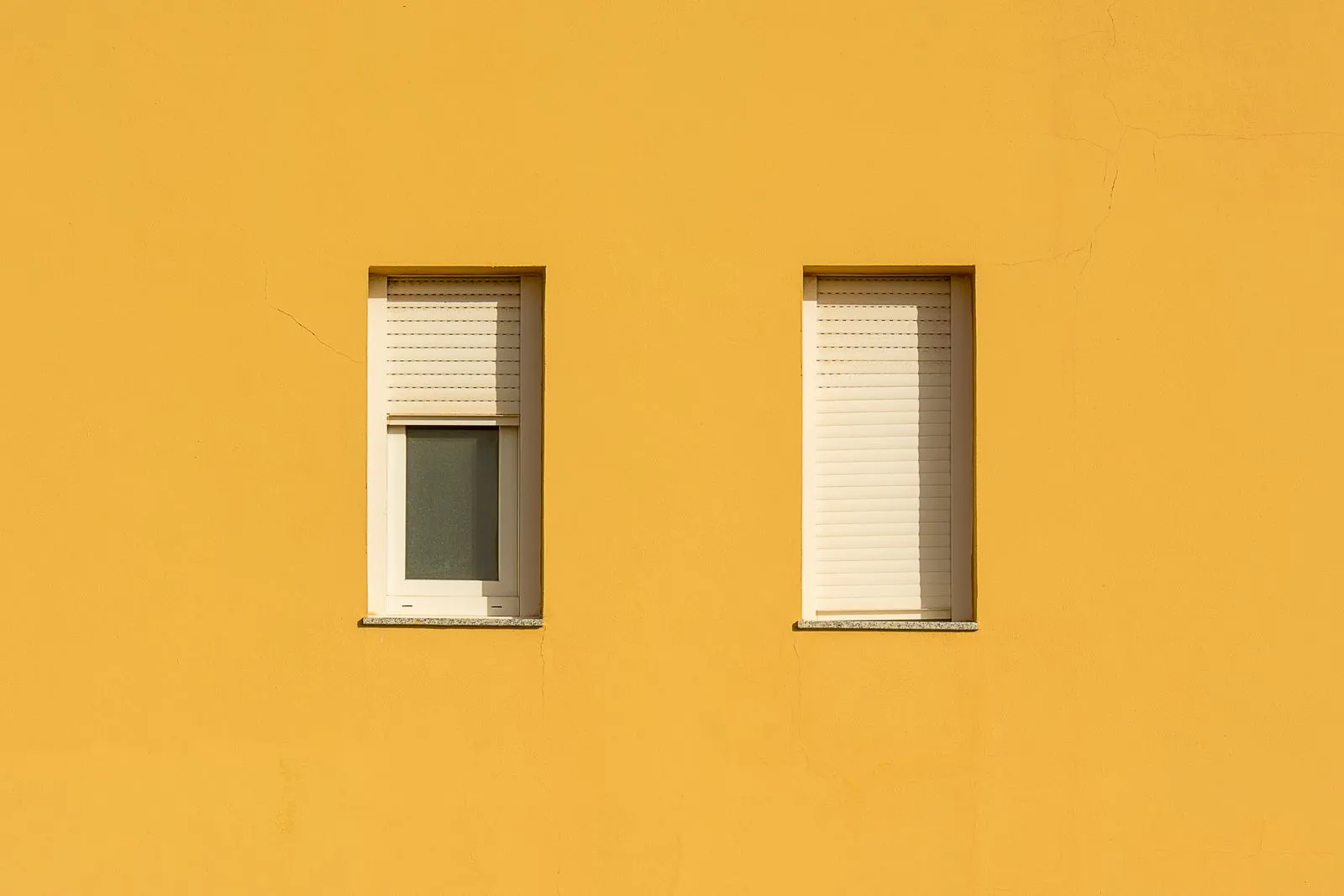 Mur jaune avec deux fenêtres et volets roulants fermés